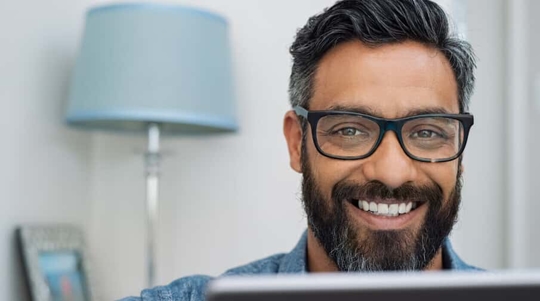 Man with dark hair and beard wearing glasses smiling